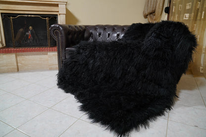 Wool Sheepskin Mongolian Blanket Throw Black - Tatifurs draped over a dark brown Chesterfield leather sofa beside a lit fireplace, long curly black Mongolian wool spilling onto the tiled floor