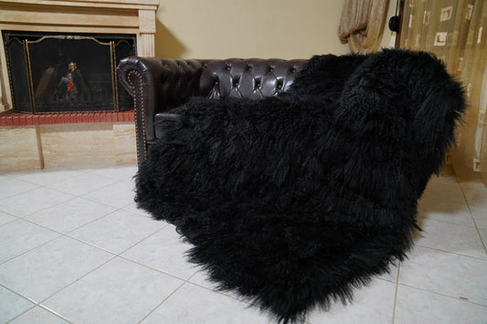 Wool Sheepskin Mongolian Blanket Throw Black - Tatifurs draped over a dark brown Chesterfield leather sofa beside a lit fireplace, long curly black Mongolian wool spilling onto the tiled floor