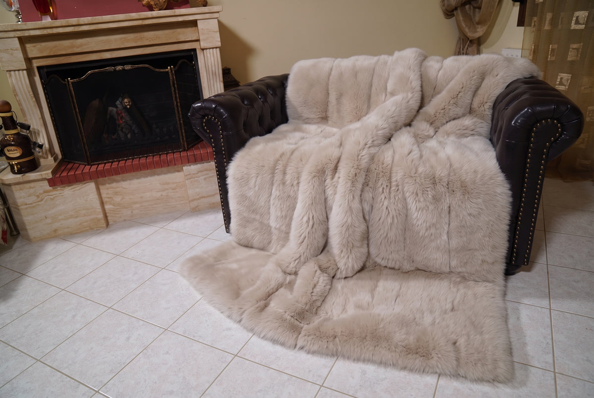 Fox Fur Blanket Throw Beige — Full Skin Saga Furs covering the back and seat of the leather armchair, fireplace behind — the warm sand beige fox skins worked head to tail, TatiFurs