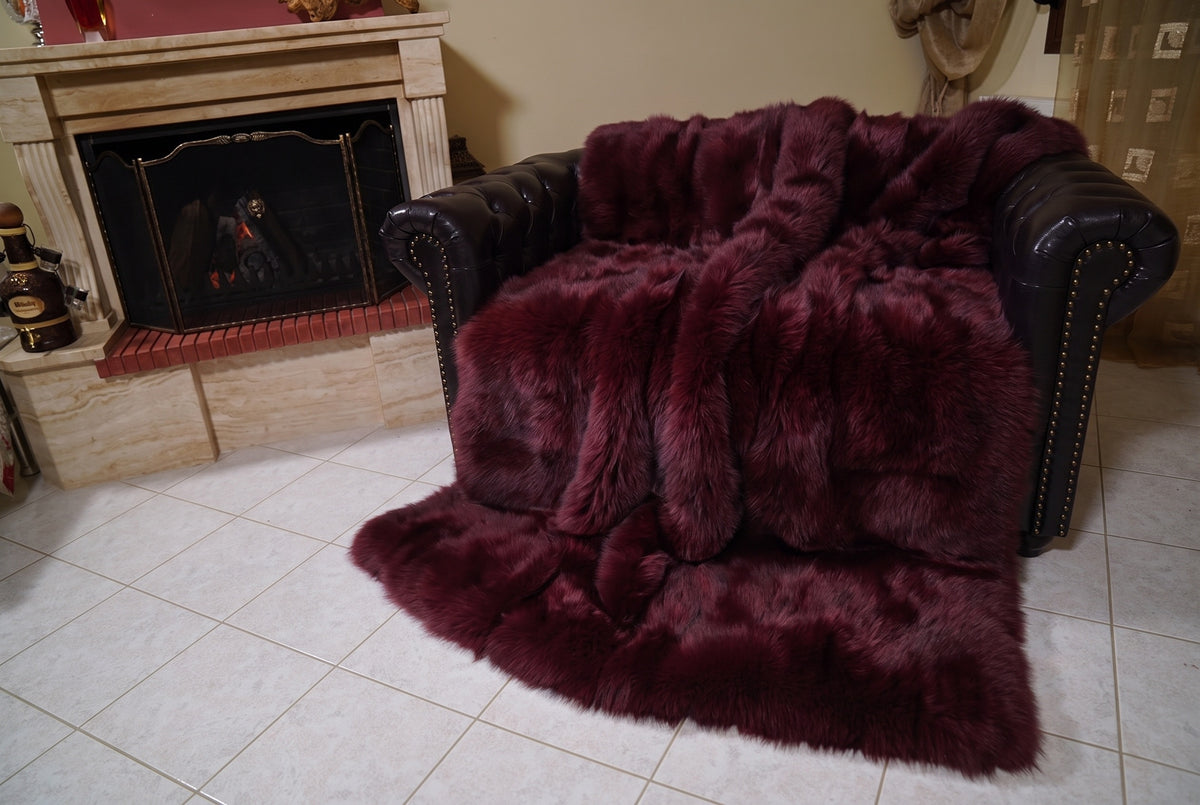 Fox Fur Blanket Throw Red Burgundy — Full Skin Saga Furs covering the back and seat of the leather armchair, fireplace behind — the deep wine burgundy fox skins worked head to tail, TatiFurs
