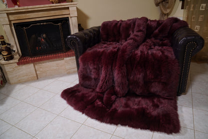 Fox Fur Blanket Throw Red Burgundy — Full Skin Saga Furs covering the back and seat of the leather armchair, fireplace behind — the deep wine burgundy fox skins worked head to tail, TatiFurs