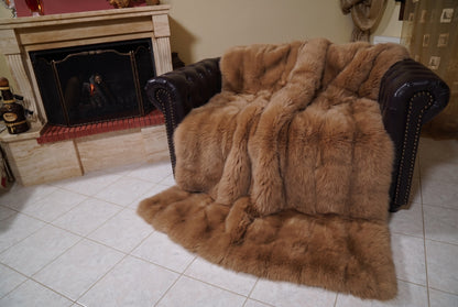 Fox Fur Blanket Throw Camel Brown — Full Skin Saga Furs covering the back and seat of the leather armchair, fireplace behind — the warm golden camel brown fox skins worked head to tail, TatiFurs