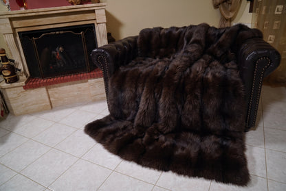 Fox Fur Blanket Throw Dark Brown — Full Skin Saga Furs covering the back and seat of the leather armchair, fireplace behind — the deep chocolate brown fox skins worked head to tail, TatiFurs