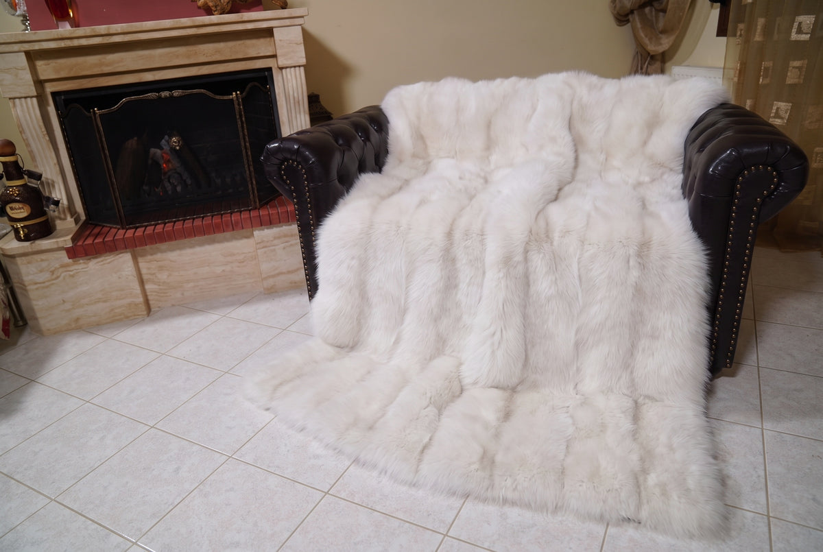 Fox Fur Blanket Throw Pearl Frost — Full Skin Saga Furs covering the back and seat of the leather armchair, fireplace behind — the pearl ivory with a soft champagne glow fox skins worked head to tail, TatiFurs