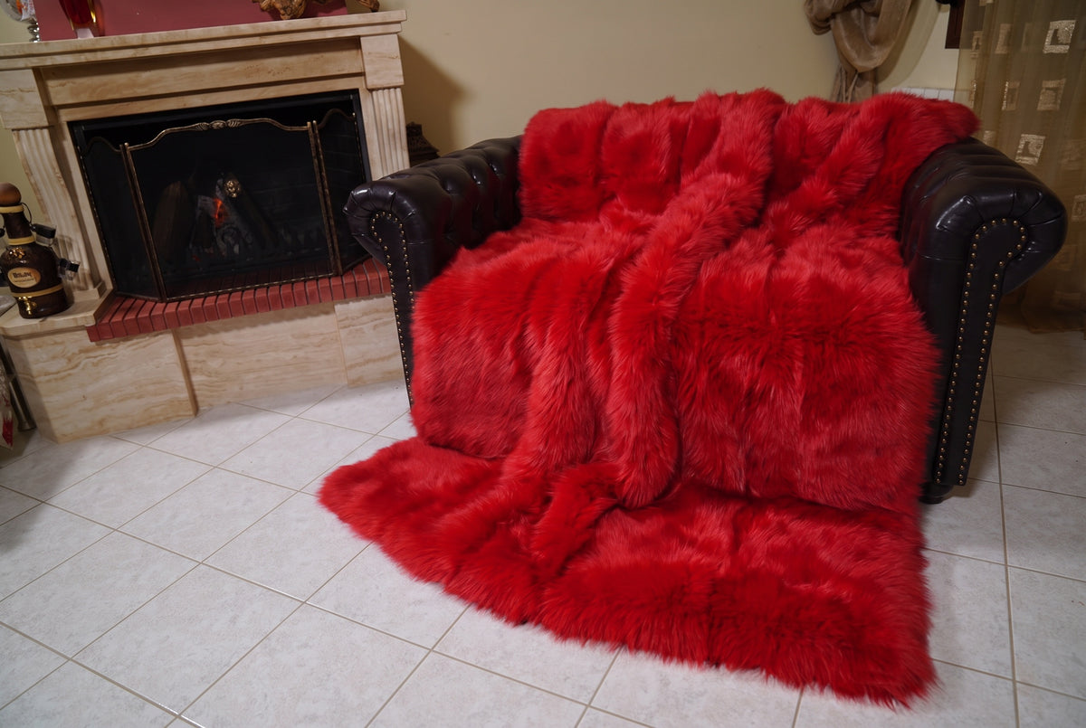 Fox Fur Blanket Throw Red — Full Skin Saga Furs covering the back and seat of the leather armchair, fireplace behind — the vivid scarlet red fox skins worked head to tail, TatiFurs