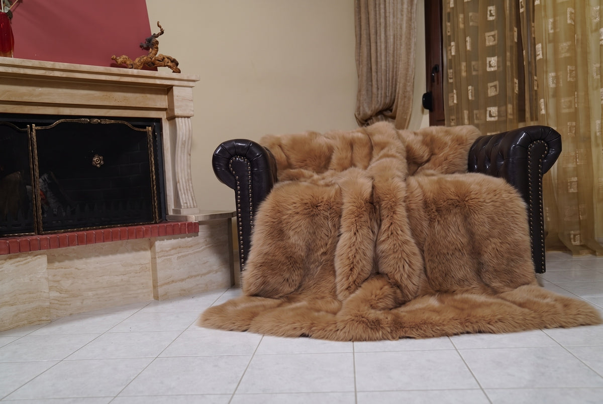 Fox Fur Blanket Throw Camel Brown — Full Skin Saga Furs draped over a dark brown leather Chesterfield armchair beside the fireplace — full view of the warm golden camel brown full skin fox pelts, TatiFurs