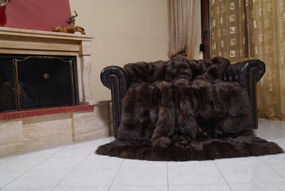 Fox Fur Blanket Throw Dark Brown — Full Skin Saga Furs draped over a dark brown leather Chesterfield armchair beside the fireplace — full view of the deep chocolate brown full skin fox pelts, TatiFurs