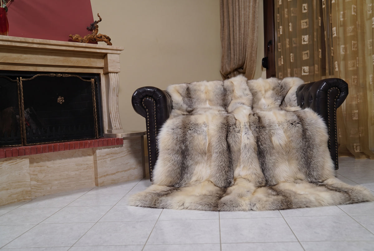 Fox Fur Blanket Throw Fawn Light — Full Skin Saga Furs draped over a dark brown leather Chesterfield armchair beside the fireplace — full view of the light fawn with a soft grey-brown line full skin fox pelts, TatiFurs