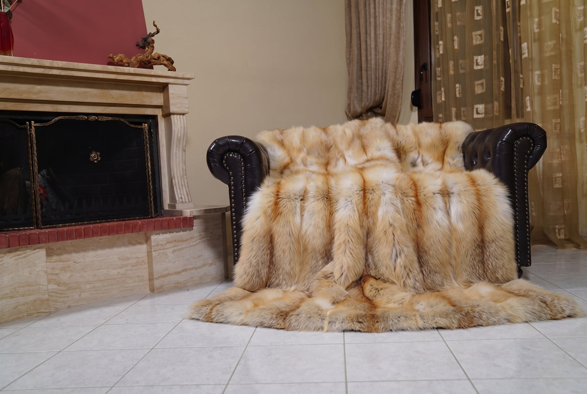 Fox Fur Blanket Throw Golden Island — Full Skin Saga Furs draped over a dark brown leather Chesterfield armchair beside the fireplace — full view of the honey-gold Golden Island full skin fox pelts, TatiFurs