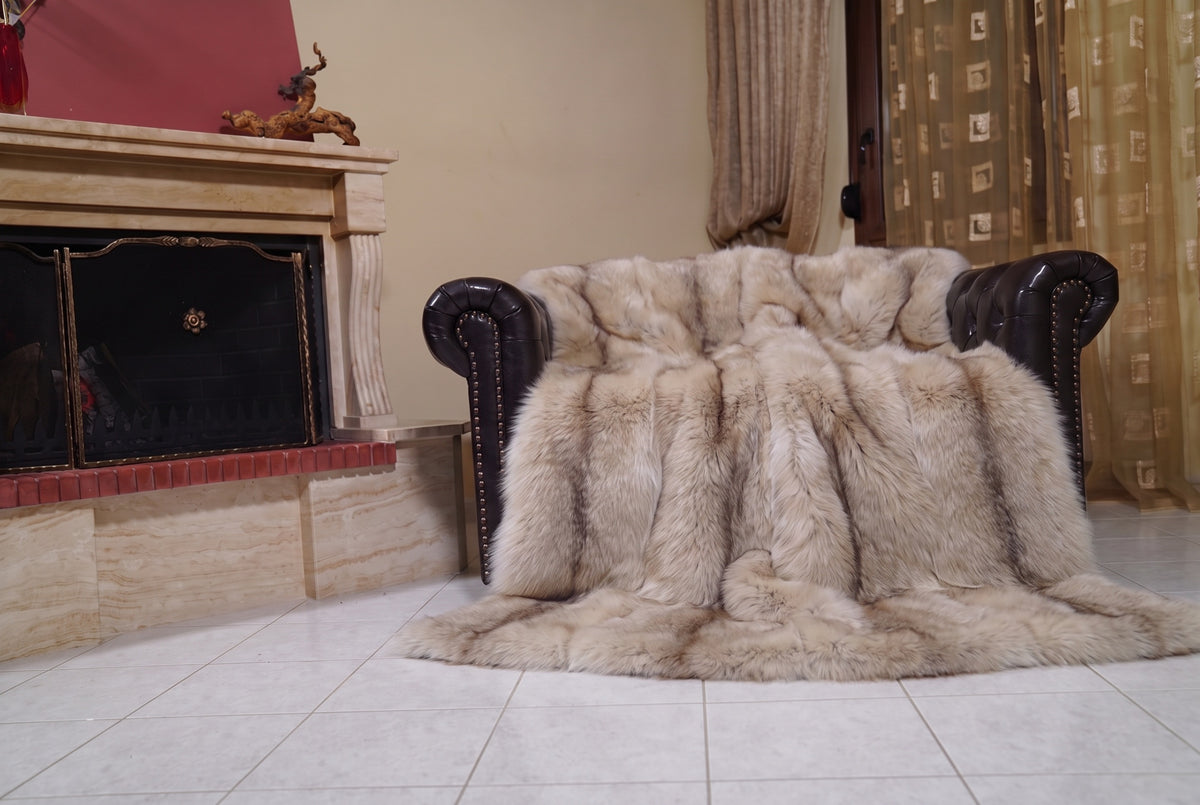Fox Fur Blanket Throw Palomino Frost — Full Skin Saga Furs draped over a dark brown leather Chesterfield armchair beside the fireplace — full view of the sand and brown Palomino Frost full skin fox pelts, TatiFurs