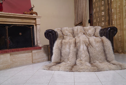 Fox Fur Blanket Throw Palomino Frost — Full Skin Saga Furs draped over a dark brown leather Chesterfield armchair beside the fireplace — full view of the sand and brown Palomino Frost full skin fox pelts, TatiFurs