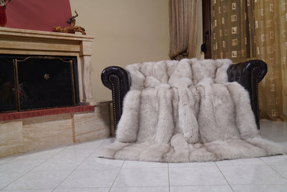Fox Fur Blanket Throw Pastel Frost — Full Skin Saga Furs draped over a dark brown leather Chesterfield armchair beside the fireplace — full view of the soft greige with a taupe line full skin fox pelts, TatiFurs
