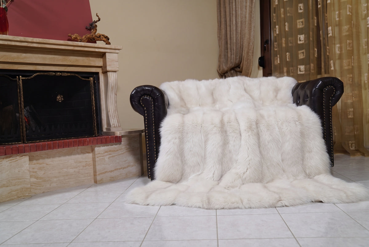 Fox Fur Blanket Throw Pearl Frost — Full Skin Saga Furs draped over a dark brown leather Chesterfield armchair beside the fireplace — full view of the pearl ivory with a soft champagne glow full skin fox pelts, TatiFurs