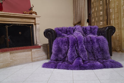 Fox Fur Blanket Throw Purple — Full Skin Saga Furs draped over a dark brown leather Chesterfield armchair beside the fireplace — full view of the rich violet purple full skin fox pelts, TatiFurs