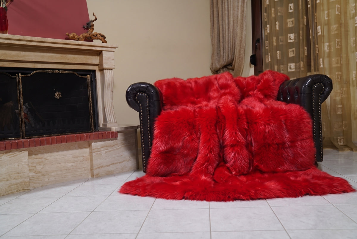 Fox Fur Blanket Throw Red — Full Skin Saga Furs draped over a dark brown leather Chesterfield armchair beside the fireplace — full view of the vivid scarlet red full skin fox pelts, TatiFurs
