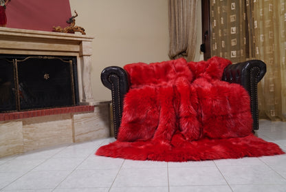 Fox Fur Blanket Throw Red — Full Skin Saga Furs draped over a dark brown leather Chesterfield armchair beside the fireplace — full view of the vivid scarlet red full skin fox pelts, TatiFurs