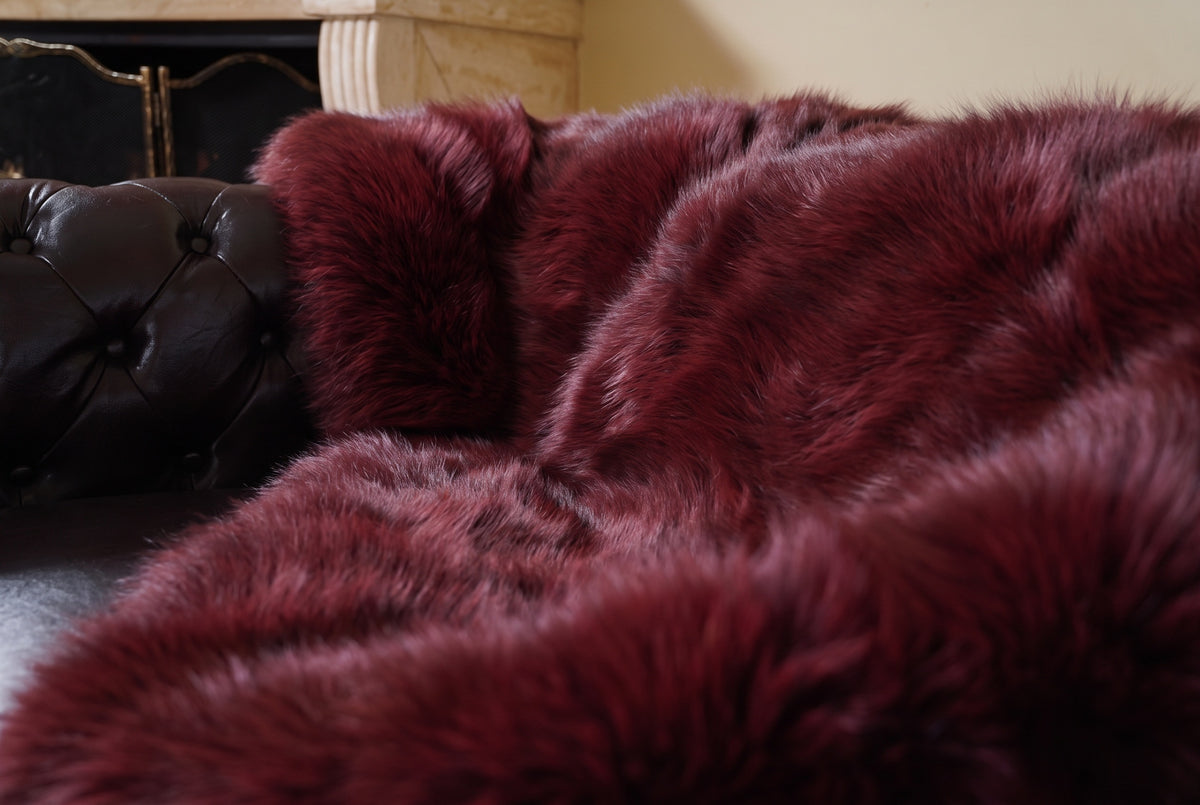 Fox Fur Blanket Throw Red Burgundy — Full Skin Saga Furs close-up of the dense deep wine burgundy fox fur texture at the edge of the armchair — Saga Furs quality, TatiFurs