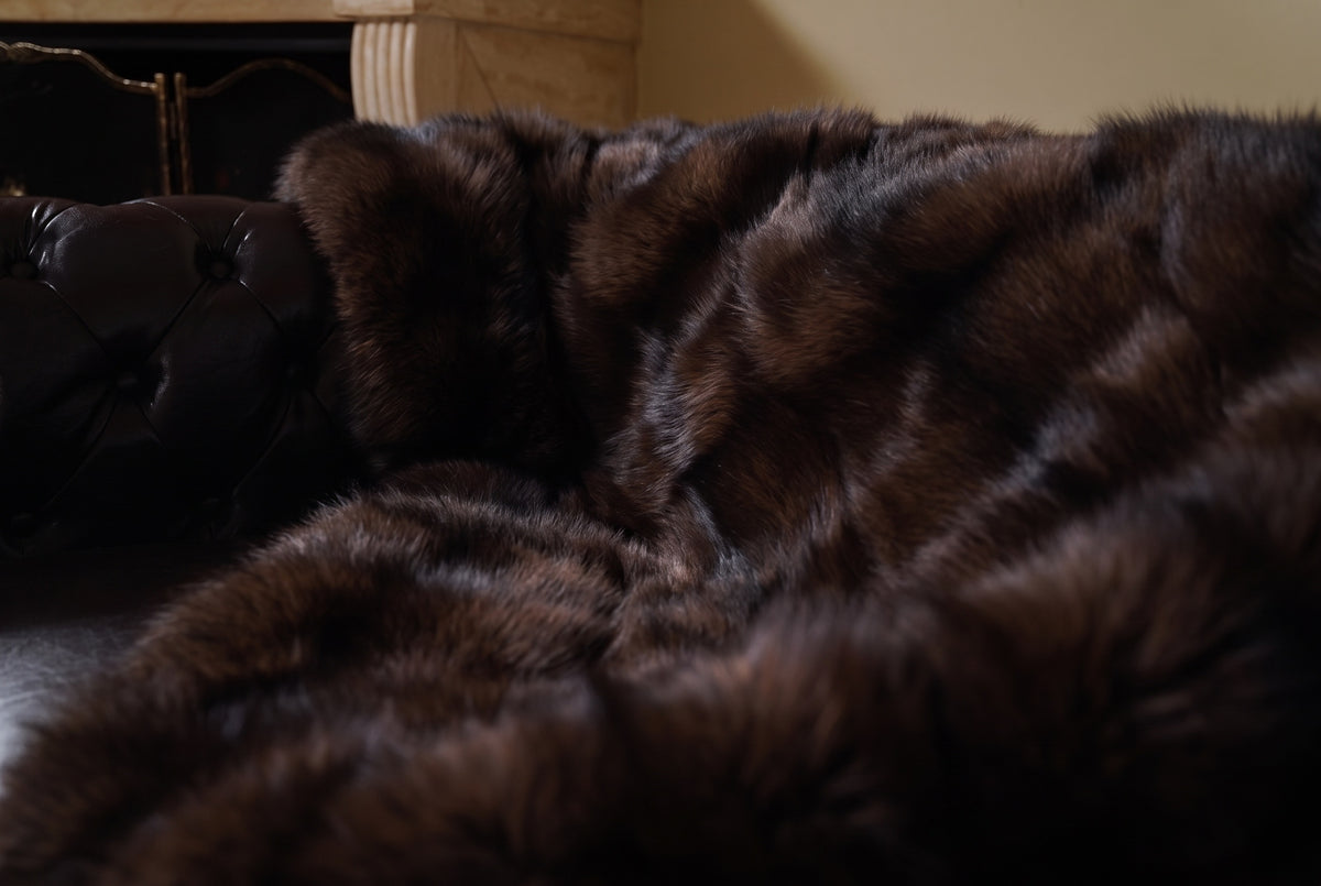 Fox Fur Blanket Throw Dark Brown — Full Skin Saga Furs close-up of the dense deep chocolate brown fox fur texture at the edge of the armchair — Saga Furs quality, TatiFurs