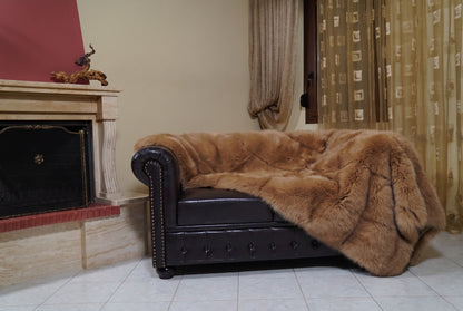 Fox Fur Blanket Throw Camel Brown — Full Skin Saga Furs on the leather armchair in a fireplace living room with curtains — warm golden camel brown real fox fur throw, TatiFurs