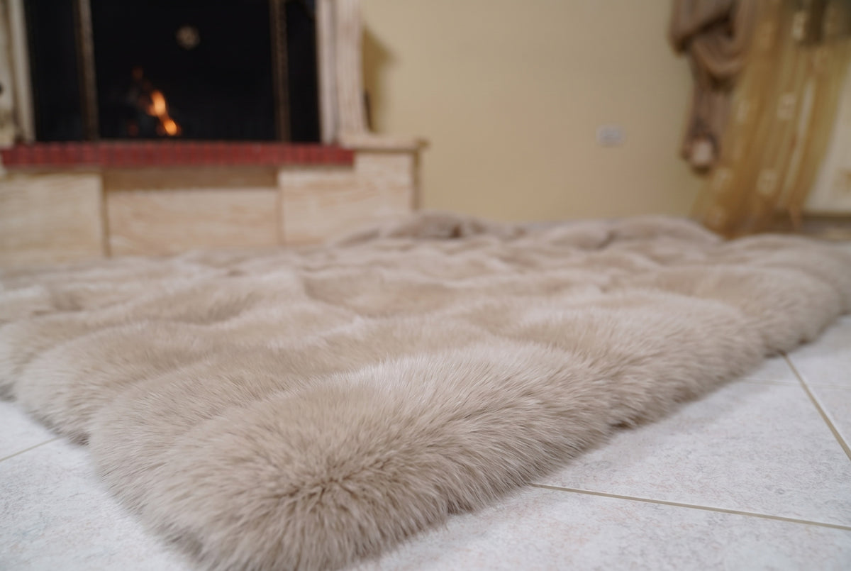Fox Fur Blanket Throw Beige — Full Skin Saga Furs laid flat on the floor in front of the lit fireplace, low angle showing the warm sand beige fox pelt rows, TatiFurs