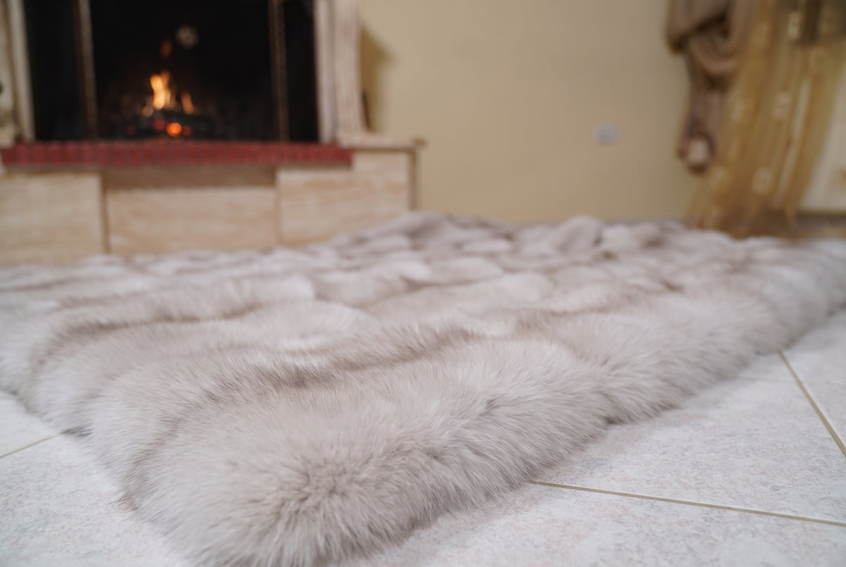 Fox Fur Blanket Throw Pastel Frost — Full Skin Saga Furs laid flat on the floor in front of the lit fireplace, low angle showing the soft greige with a taupe line fox pelt rows, TatiFurs