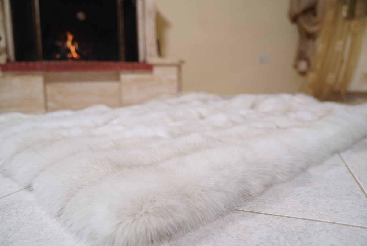 Fox Fur Blanket Throw Pearl Frost — Full Skin Saga Furs laid flat on the floor in front of the lit fireplace, low angle showing the pearl ivory with a soft champagne glow fox pelt rows, TatiFurs