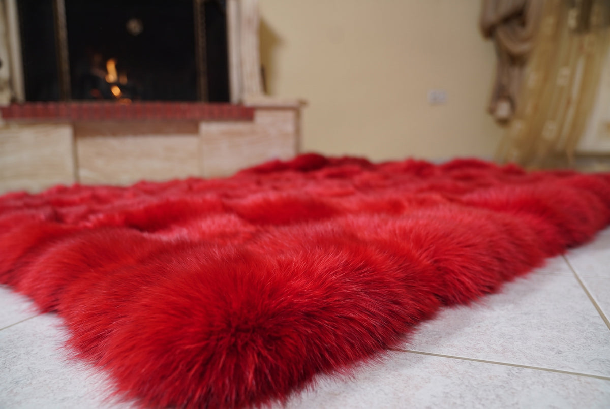 Fox Fur Blanket Throw Red — Full Skin Saga Furs laid flat on the floor in front of the lit fireplace, low angle showing the vivid scarlet red fox pelt rows, TatiFurs