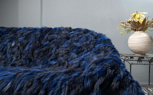 Luxury electric blue and black fox fur blanket draped over a dark sofa showing vivid charged colour contrast
