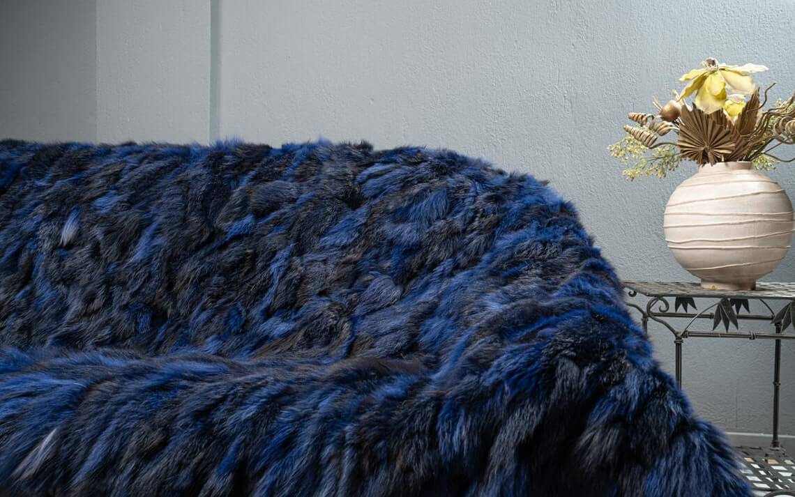 Fox Fur Blanket Throw Blue Electric - Tatifurs draped over a couch, showcasing its vibrant electric blue and black hues.