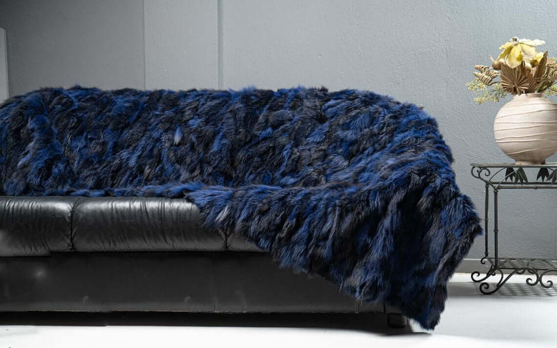 Fox Fur Blanket Throw Blue Electric - Tatifurs draped on a black leather couch, showcasing its vibrant color and luxurious texture.