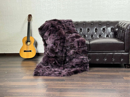 Purple fox fur blanket with black details draped across a bed showing dramatic colour and natural fur volume
