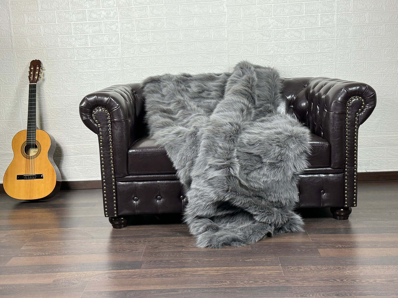 Fox Fur Blanket Throw Grey - Tatifurs draped over a leather couch, showcasing its luxurious gray fox fur texture.