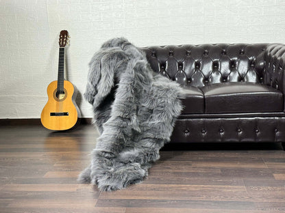 Fox Fur Blanket Throw Grey - Tatifurs draped on a leather couch beside a guitar, showcasing its luxurious softness.
