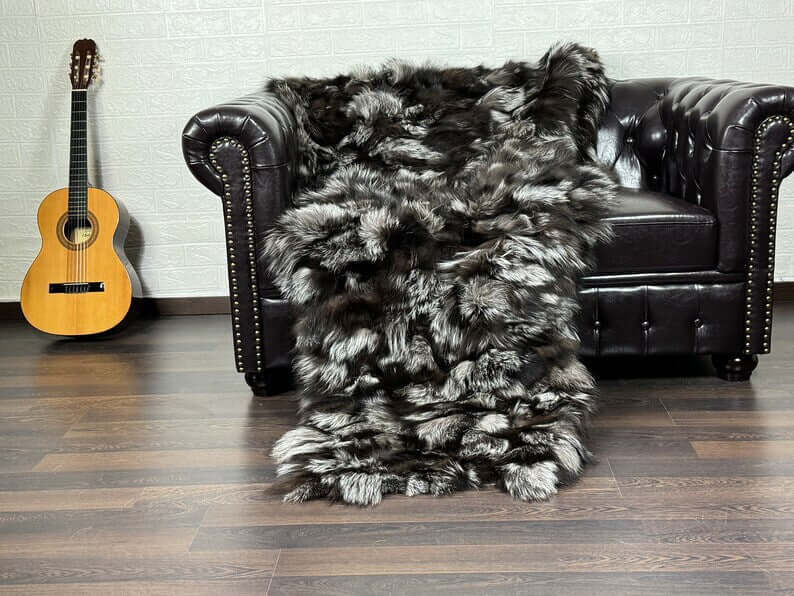Fox Fur Blanket Throw Silver - Tatifurs draped over a black leather couch, showcasing its luxurious silver fox fur texture.