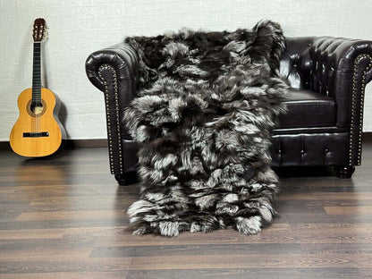 Fox Fur Blanket Throw Silver - Tatifurs draped over a black leather couch, showcasing its luxurious silver fox fur texture.