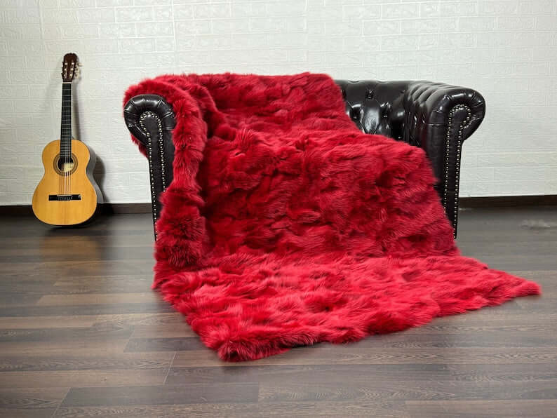 Fox Fur Blanket Throw Red - Tatifurs draped on a leather couch next to a guitar, showcasing vibrant red color.