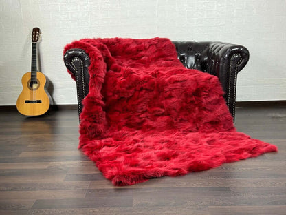 Fox Fur Blanket Throw Red - Tatifurs draped on a leather couch next to a guitar, showcasing vibrant red color.