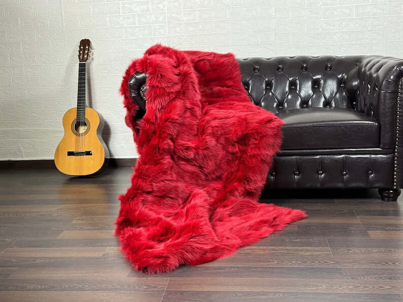 Fox Fur Blanket Throw Red - Tatifurs draped over a black leather couch next to a guitar.