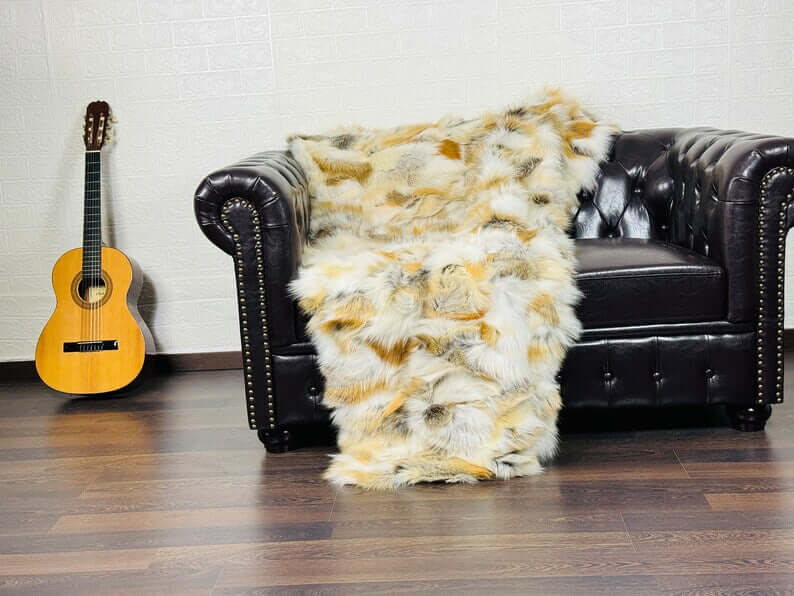 Fox Fur Blanket Throw Golden - Tatifurs draped over a black leather couch next to a guitar.