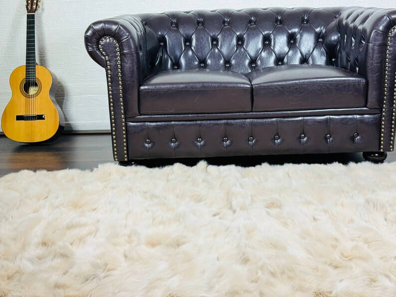 Fox Fur Blanket Throw Beige - Tatifurs on a cozy living room floor with a dark leather couch and a guitar.