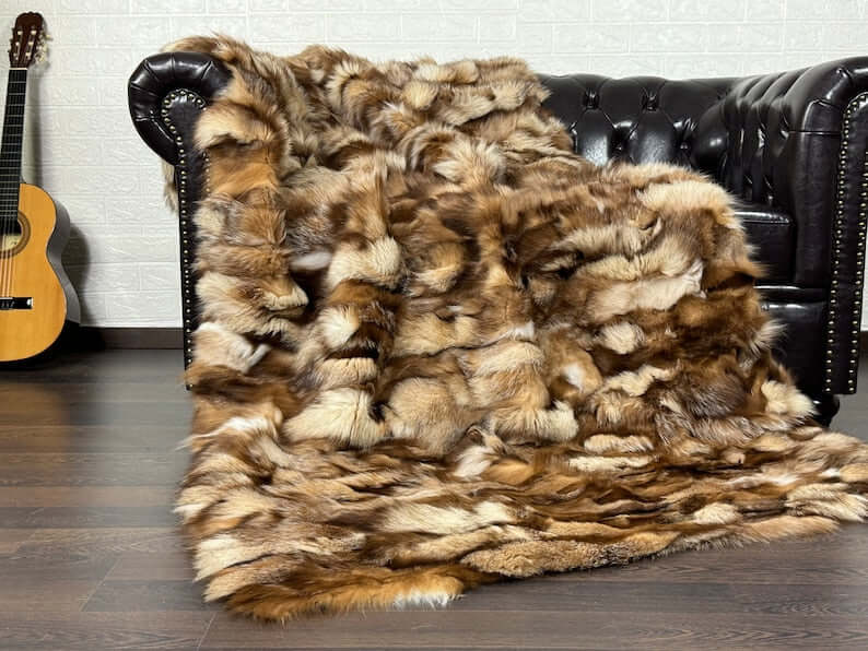 Fox Fur Blanket Throw Crystal Natural - Tatifurs draped on a leather sofa, showcasing its luxurious texture and colors.