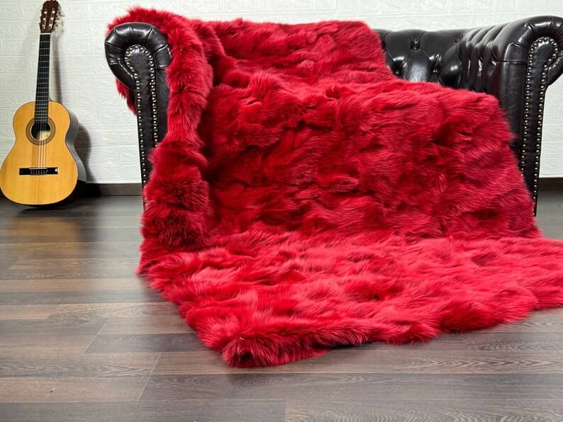 Fox Fur Blanket Throw Red - Tatifurs draped over a black leather couch in a cozy setting.