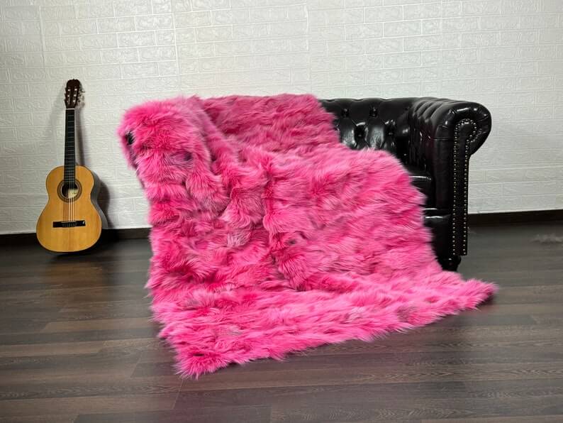 Fox Fur Blanket Throw Fuchsia - Tatifurs displayed on a couch next to a guitar, showcasing bold fuchsia design.