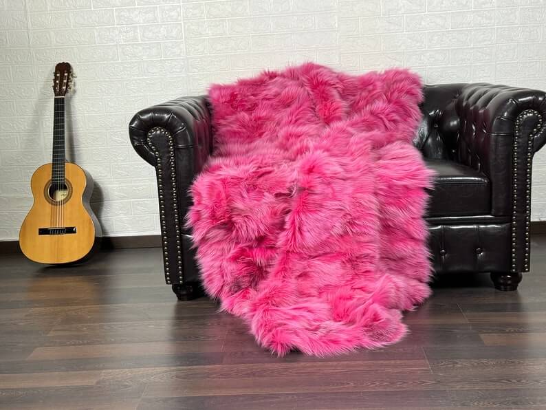 Fox Fur Blanket Throw Fuchsia - Tatifurs draped on a leather couch next to a guitar, showcasing its luxurious color and texture.
