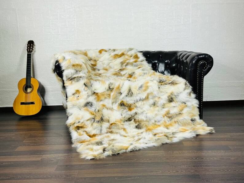 Fox Fur Blanket Throw Golden - Tatifurs draped over a black leather couch with a guitar in the background.