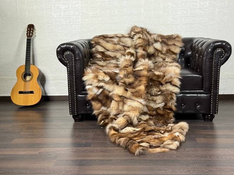 Fox Fur Blanket Throw Crystal Natural - Tatifurs draped on a dark leather couch next to a guitar.