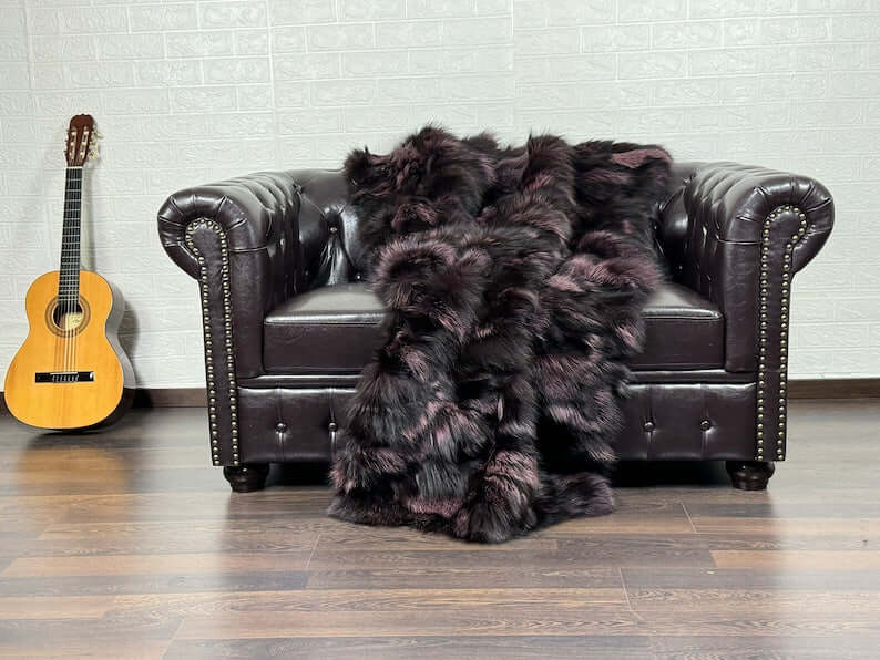 Fox Fur Blanket Throw Black Purple - Tatifurs draped on a leather couch, showcasing its luxurious texture and rich colors.