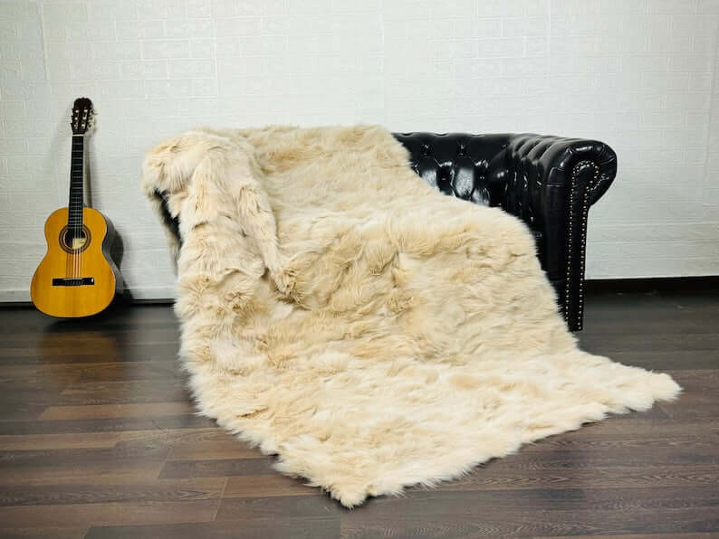 Fox Fur Blanket Throw Beige - Tatifurs draped on a black leather couch with a guitar in the background.