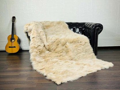 Fox Fur Blanket Throw Beige - Tatifurs draped on a black leather couch with a guitar in the background.