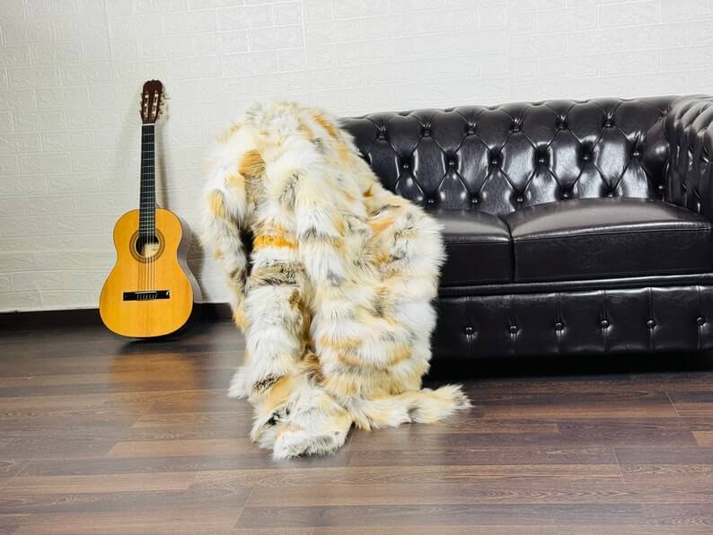 Fox Fur Blanket Throw Golden - Tatifurs draped over a black leather sofa with a guitar in the background.
